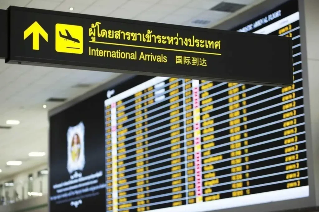 Illuminated International Arrivals directional sign and flight information display board inside an airport terminal.