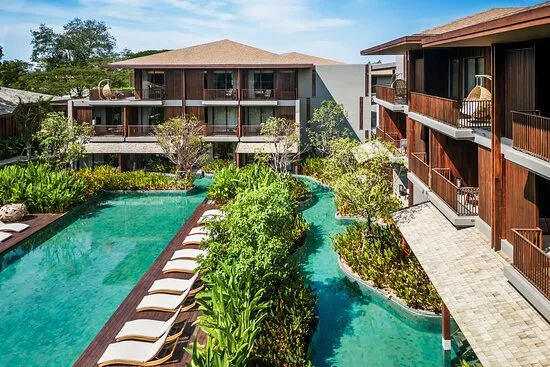 Beautiful tranquil swimming pool surrounded by tropical gardens and wooden luxury resort buildings at Andaz Pattaya Jomtien Beach.