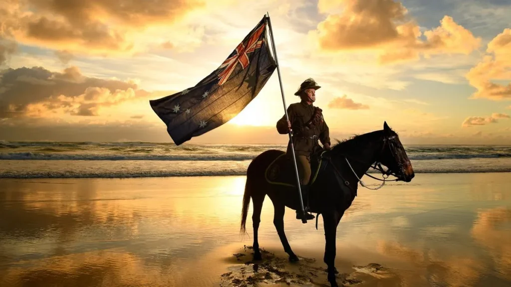 Anzac Day tribute showing an Australian soldier in uniform riding a horse and holding the Australian flag on a beach at sunrise.
