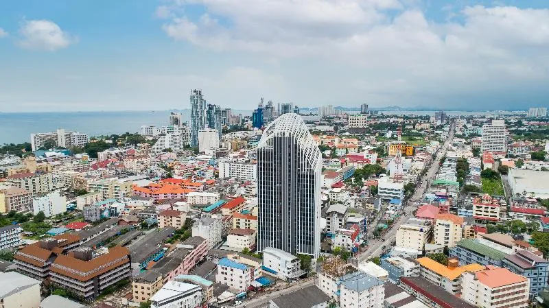 Aerial daytime view of Arbour Hotel and Residence Pattaya, a tall modern building standing out in the middle of Pattaya city, with the ocean in the background.