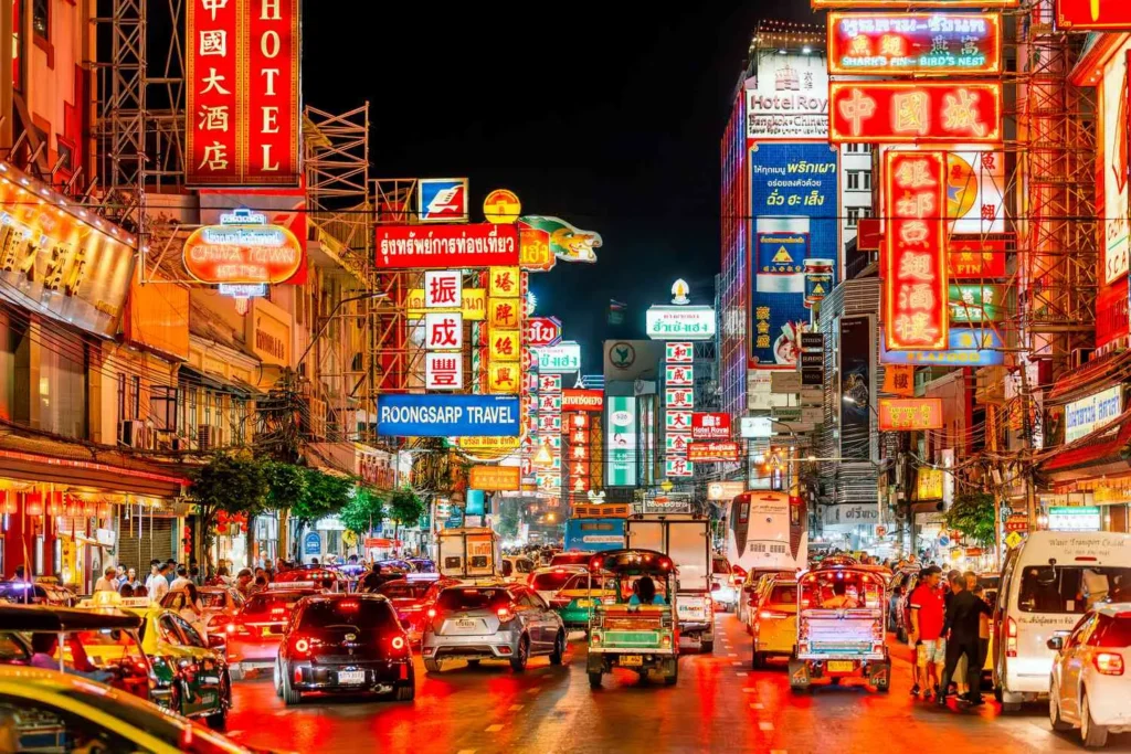 Vibrant nightlife and heavy traffic on Yaowarat Road in Bangkok's Chinatown, beautifully illuminated by colorful neon signs.