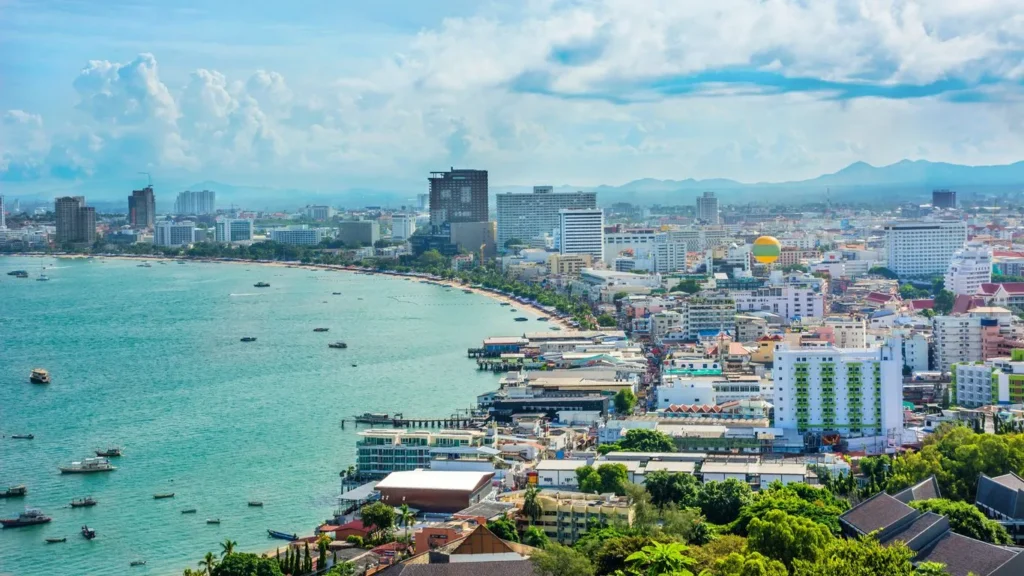 High-angle aerial view of Pattaya Bay showing the crescent-shaped beach, turquoise sea, and coastal city buildings.