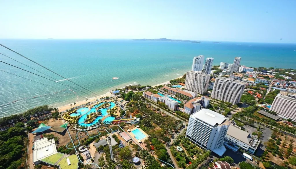 High-angle aerial view of a beach resort in Pattaya, featuring a large water park, hotels, and a curved coastline alongside the ocean.