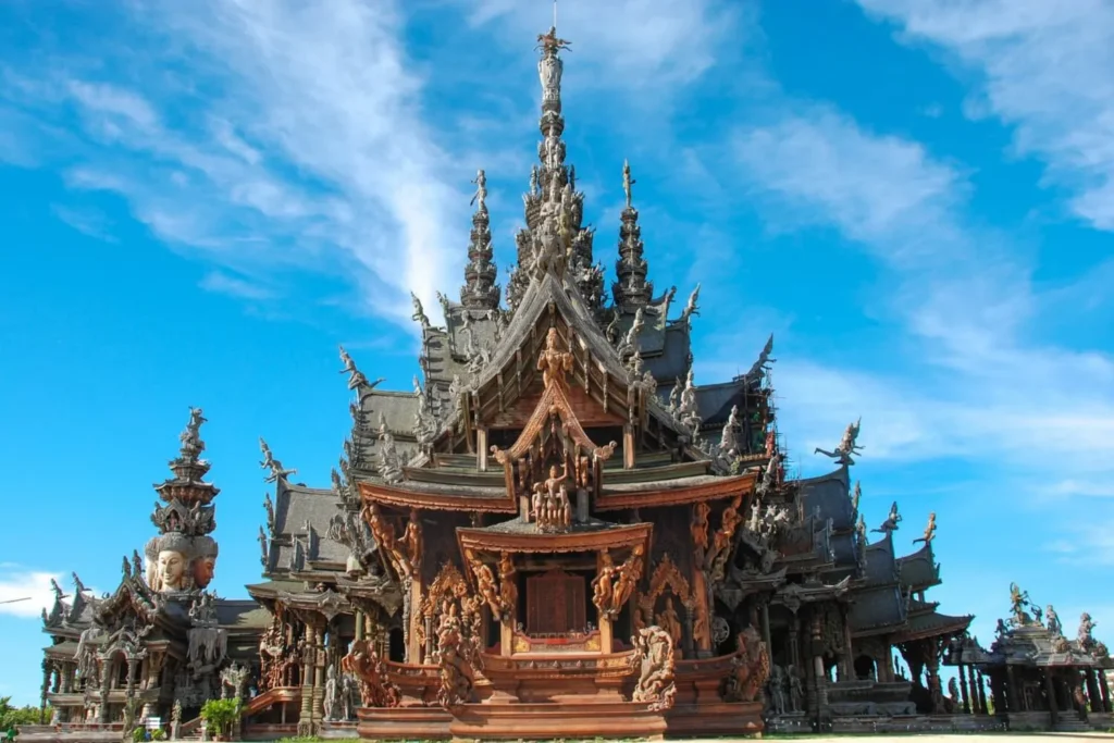 Detailed exterior view of the Sanctuary of Truth, a magnificent intricately carved wooden temple in Pattaya, Thailand, set against a bright blue sky.
