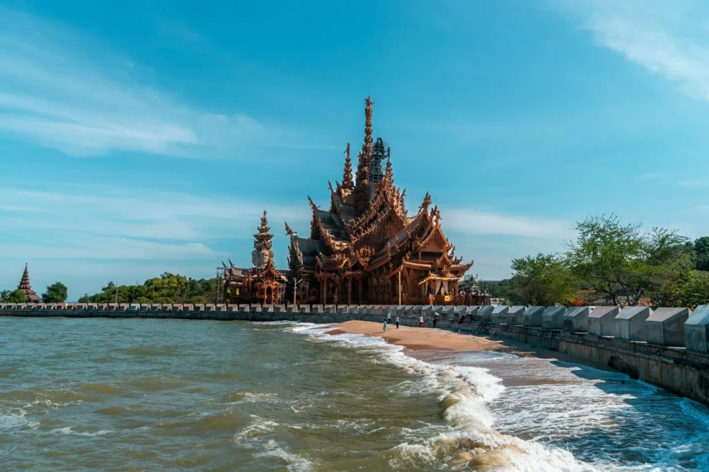 The majestic Sanctuary of Truth, an intricately carved wooden temple located right on the coastline of Pattaya, Thailand, under a clear blue sky.