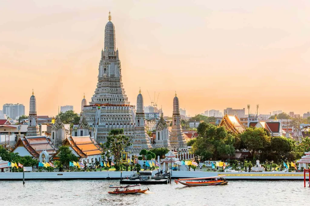 Beautiful daytime view of Wat Arun, the Temple of Dawn, situated along the Chao Phraya River in Bangkok with traditional longtail boats passing by.