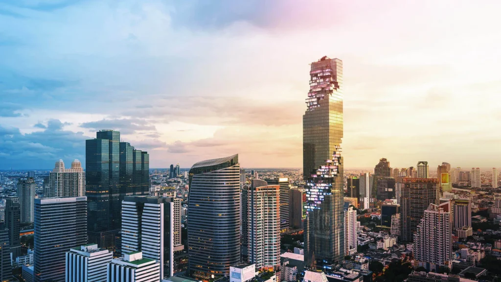 The iconic pixelated architecture of the King Power Mahanakhon building standing out in the Bangkok city skyline during a colorful sunset.