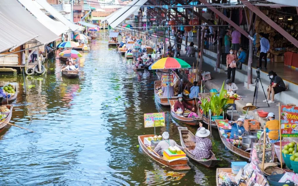 Bustling cultural scene at the Pattaya Floating Market featuring vendors selling local food from traditional wooden boats along the canal, surrounded by tourists on wooden walkways.