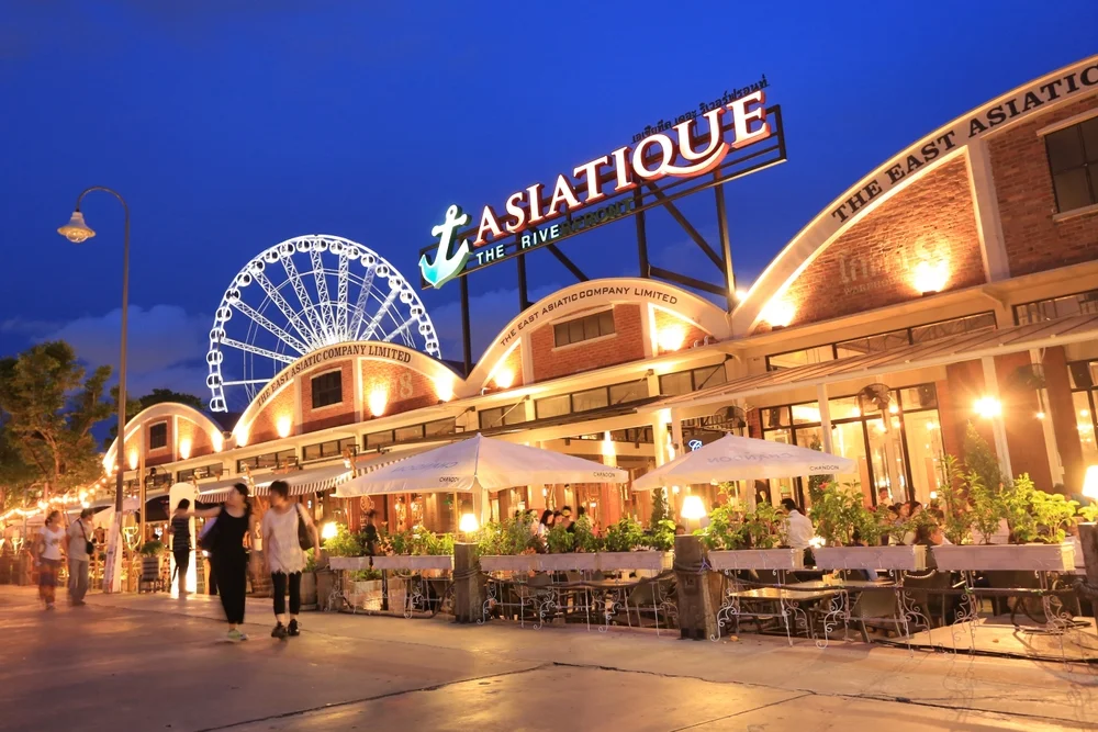 illuminated Asiatique The Riverfront sign and Ferris wheel at dusk with outdoor dining restaurants in Bangkok, Thailand.