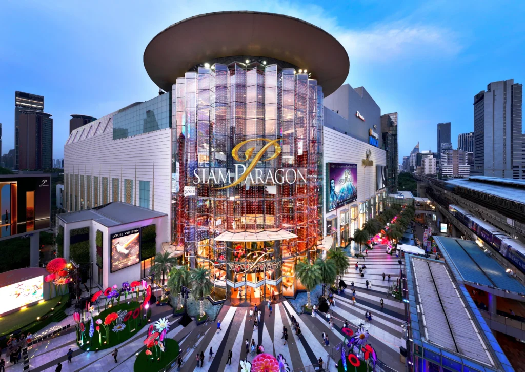 Majestic twilight exterior view of the iconic glass entrance structure and plaza at Siam Paragon luxury shopping mall in downtown Bangkok.