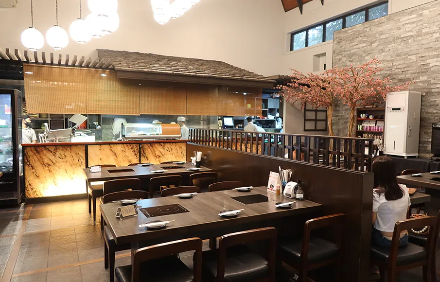 Warm and modern wooden interior design of Suki Masa Japanese sukiyaki restaurant with dining tables and an open kitchen counter.