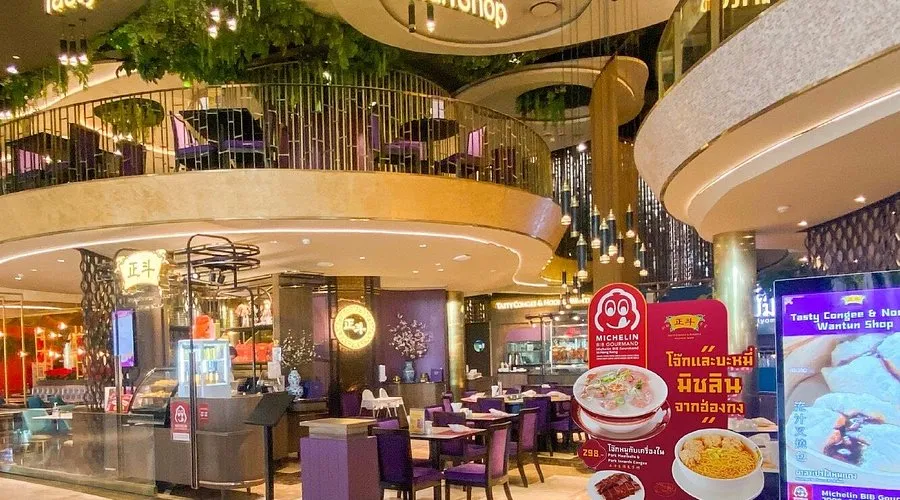 The elegant two-story interior of Tasty Congee and Noodle Wantun Shop featuring purple seating and a Michelin Bib Gourmand promotional sign at the entrance.